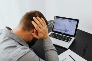 man with laptop on desk terrified by stock market chart