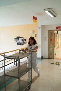 smiling caregiver with an empty serving cart in the corridor of a nursing home